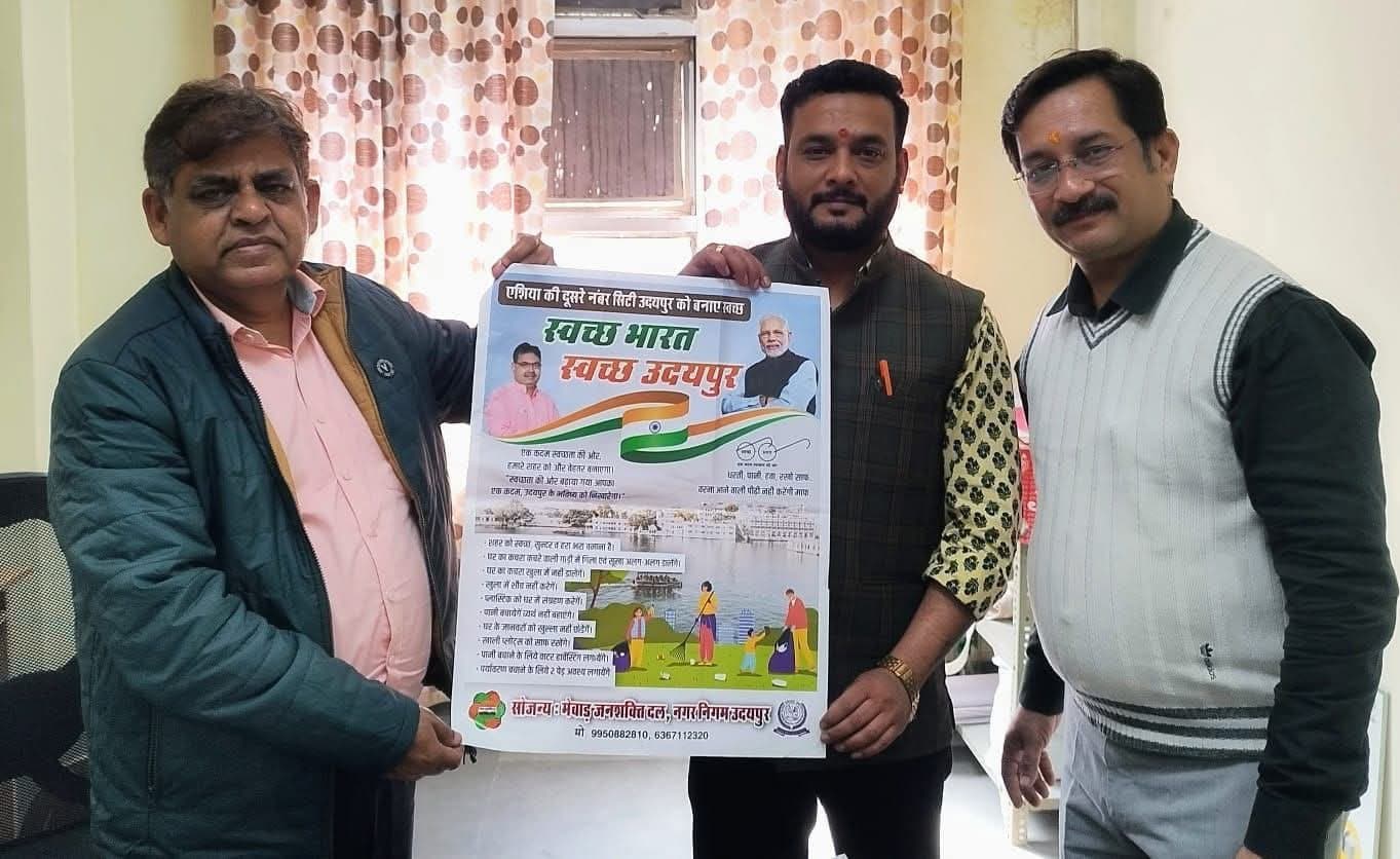 Three men hold up the ‘स्वच्छ भारत स्वच्छ उदयपुर’ poster by Mewar Jan Shakti Dal and Nagar Nigam Udaipur in an office