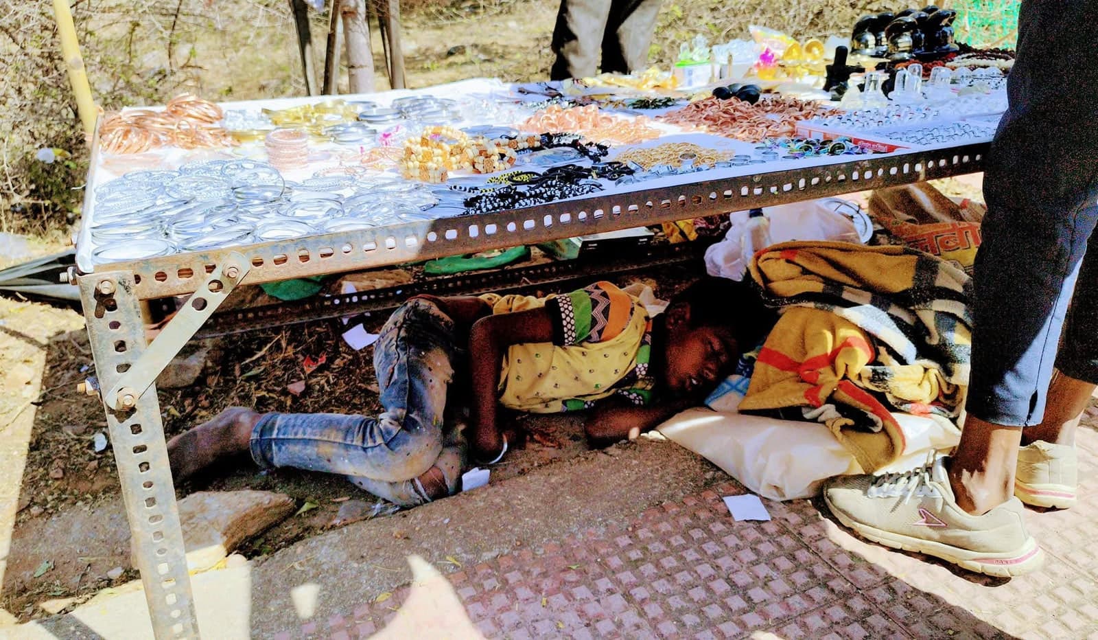 A young child asleep on the ground beneath a roadside stall selling bangles